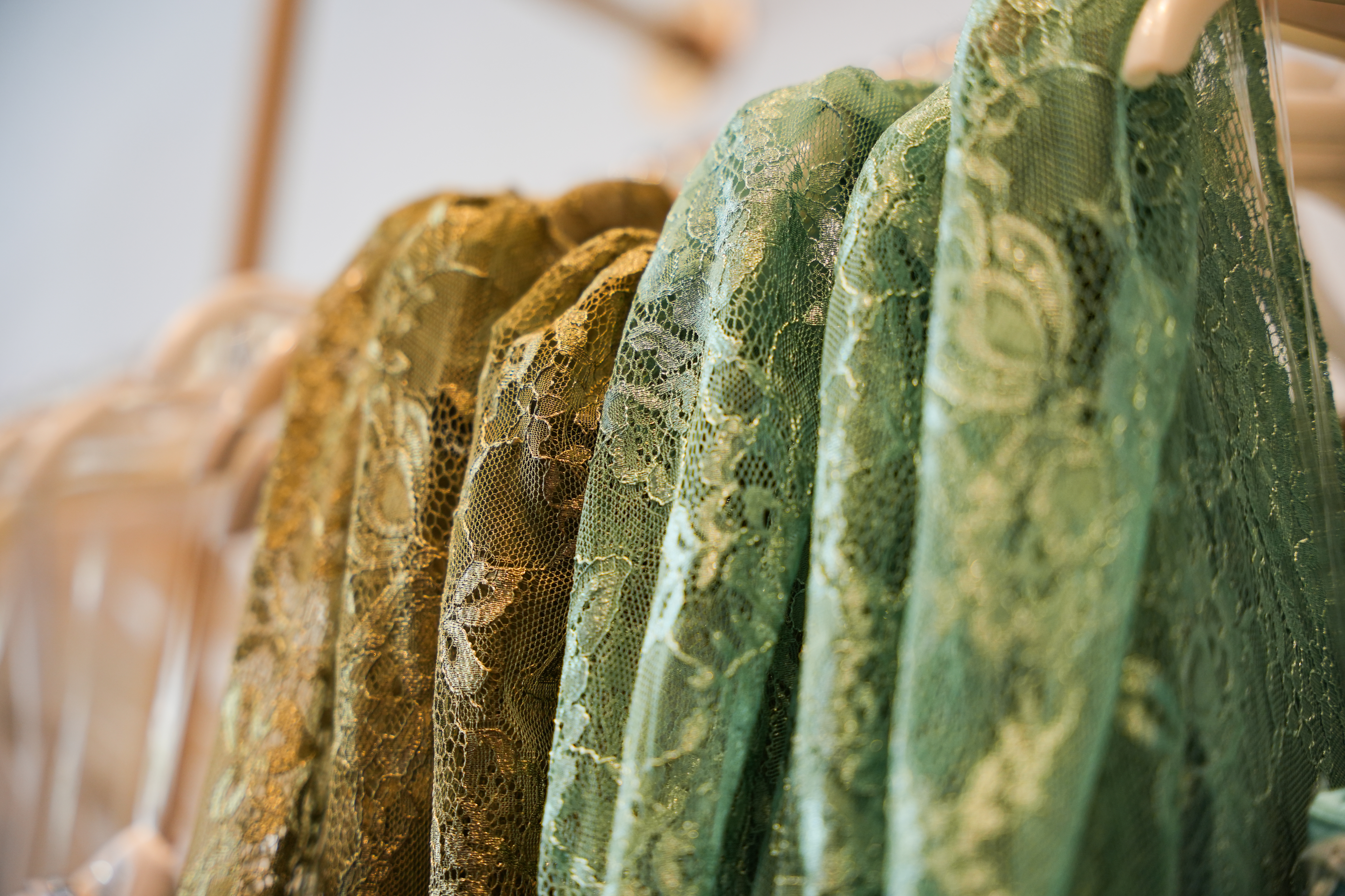 Nahaufnahme von grüner und goldener Spitze auf Kleidern bei Arya Mode